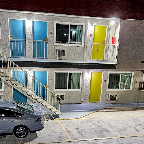 The image shows a motel with colorfully painted doors, two parked cars, and a flight of stairs connecting the first and second floors.