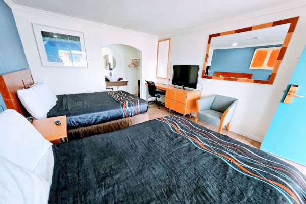 A modern hotel room with two beds, desk, chair, and a TV. There's a large mirror and a painting on the wall.